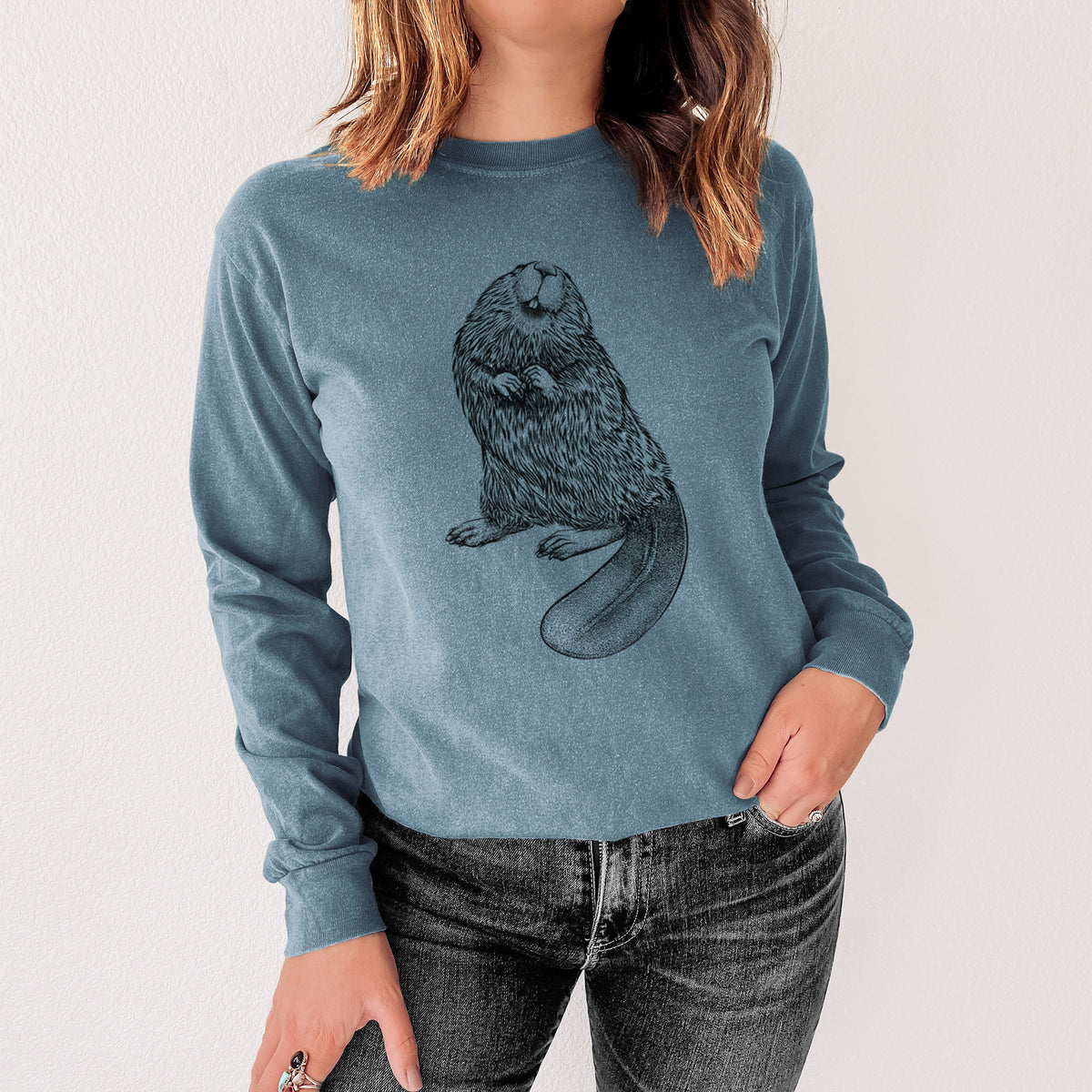 Steel blue Comfort Colors long sleeve shirt printed with a detailed black ink illustration of an American beaver sitting upright with its flat tail, shown in a lifestyle photo.
