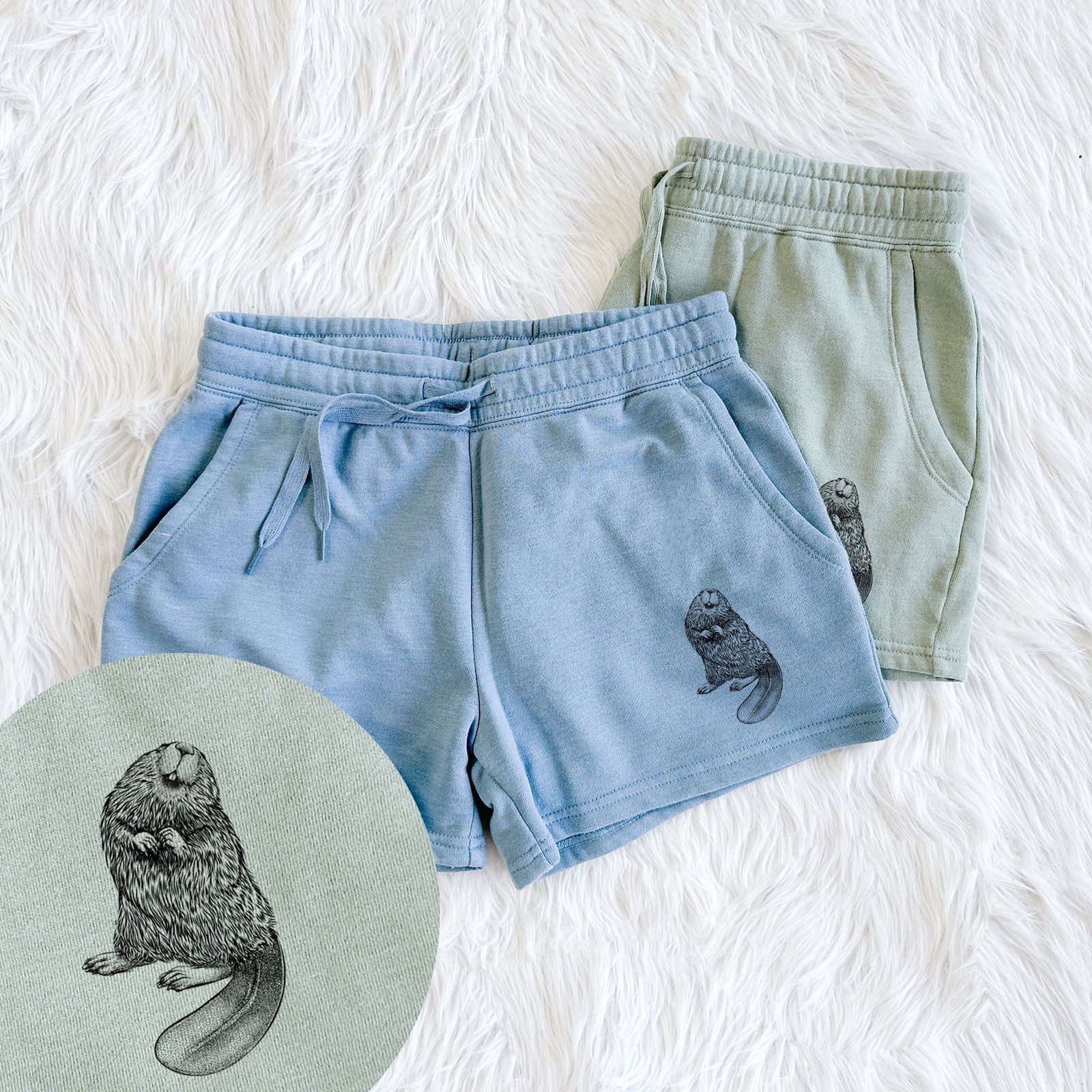 Two pairs of Cali Wave shorts in different colors printed with a detailed black ink illustration of an American beaver sitting upright with its flat tail, with a close-up of the print.