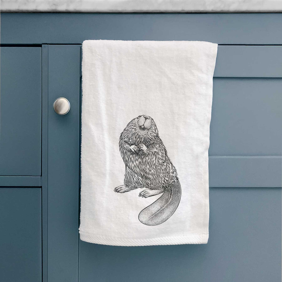 White hand towel printed with a detailed black ink illustration of an American beaver sitting upright with its flat tail, hanging on a cabinet door.
