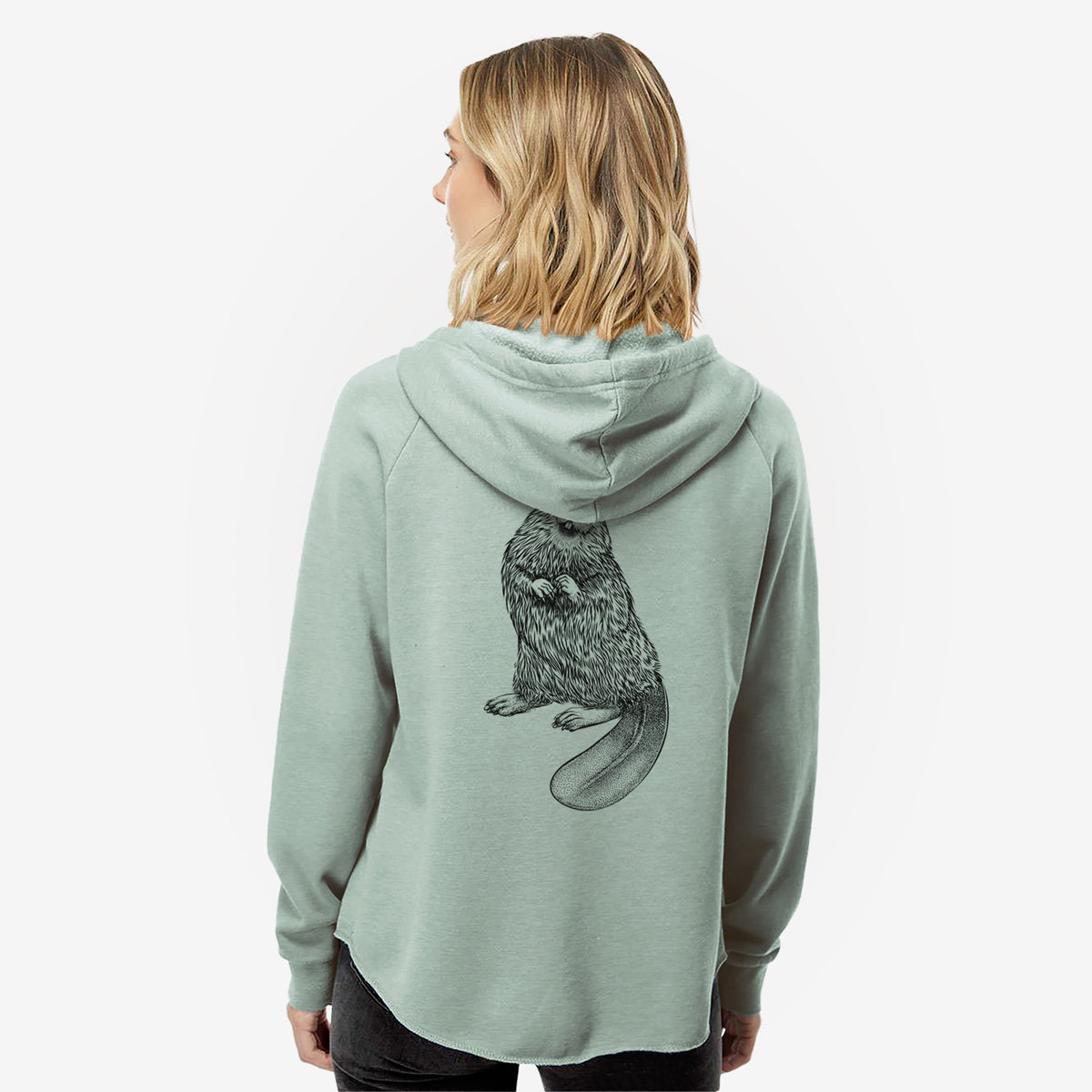 Woman wearing a sage green women's Cali Wave zip-up sweatshirt printed with a detailed black ink illustration of an American beaver sitting upright with its flat tail, seen from behind.