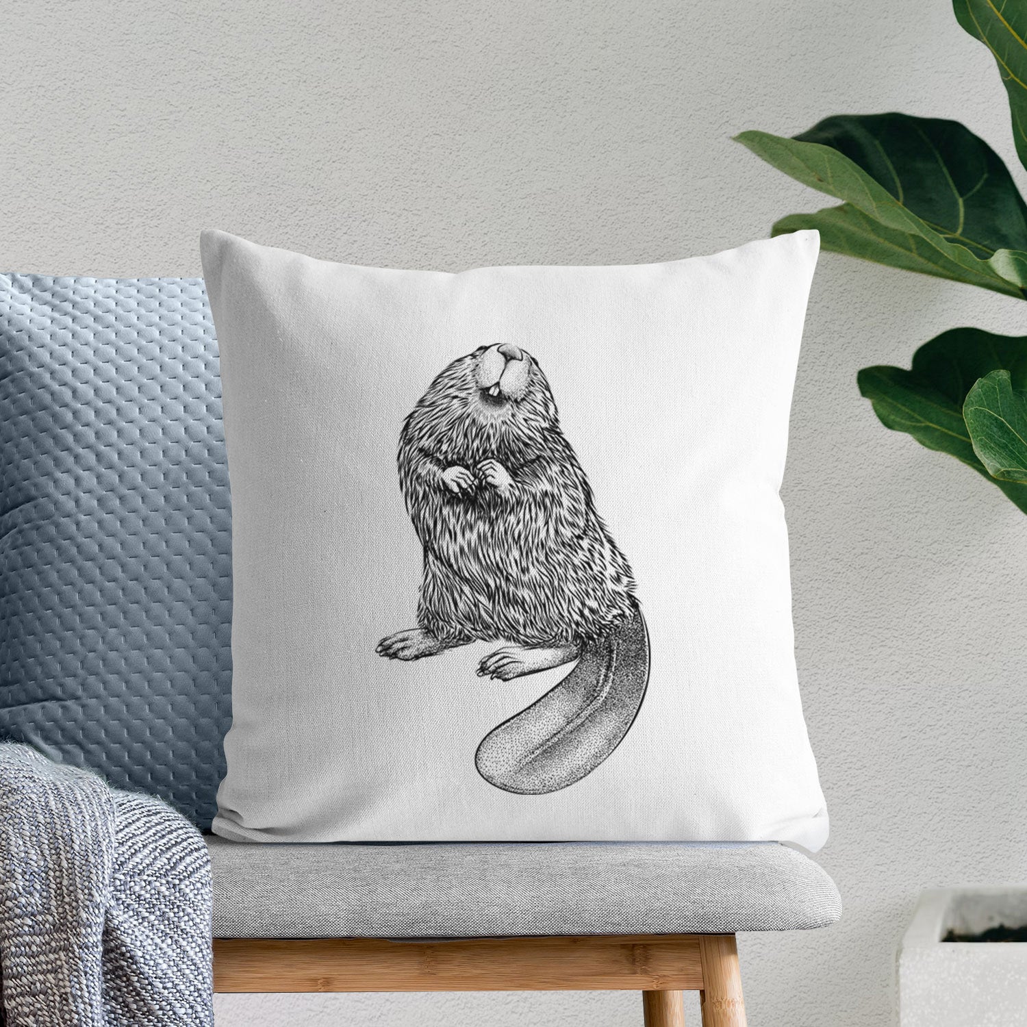White pillow cover printed with a detailed black ink illustration of an American beaver sitting upright with its flat tail, on a bench beside plants.