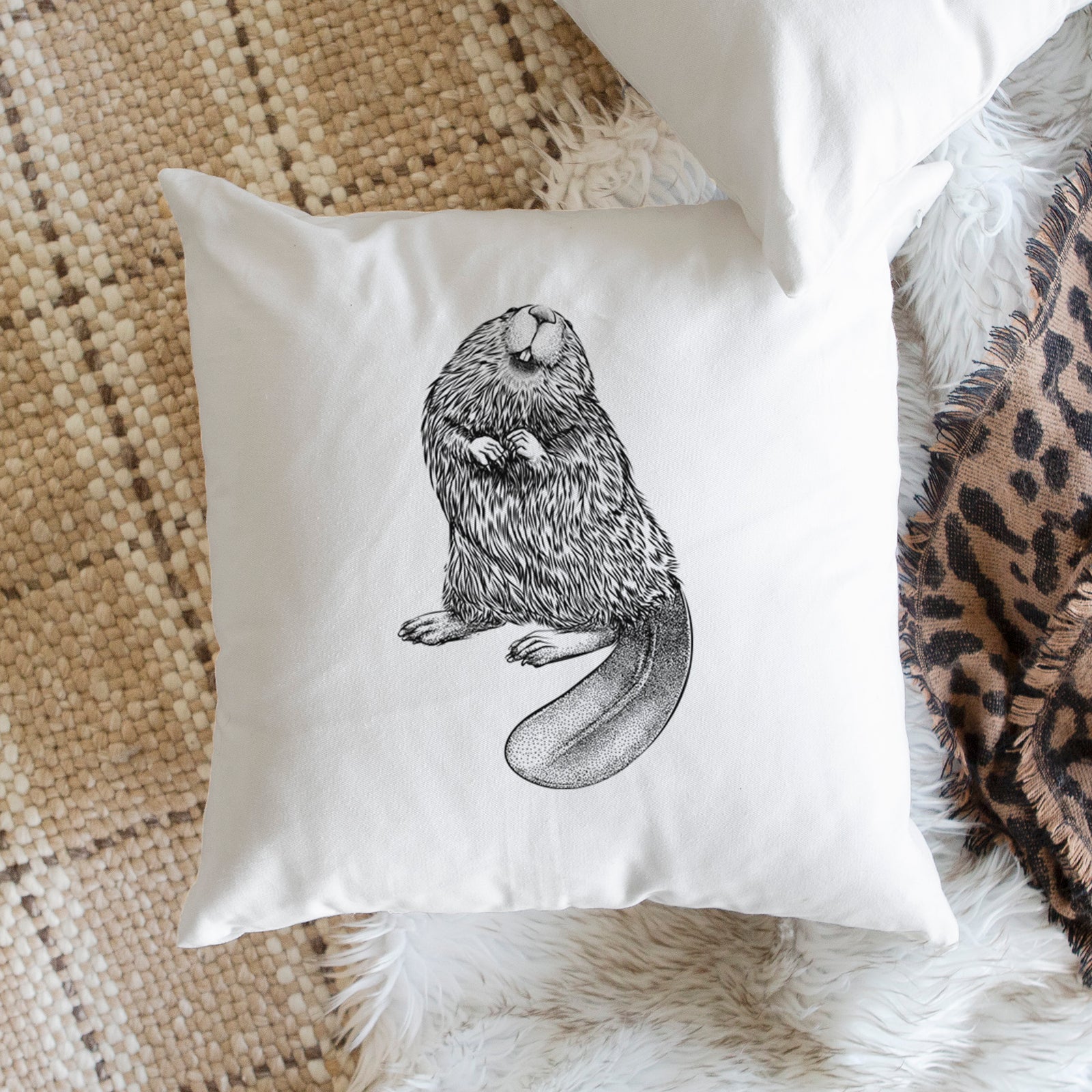 White pillow cover printed with a detailed black ink illustration of an American beaver sitting upright with its flat tail, on a bench beside plants.