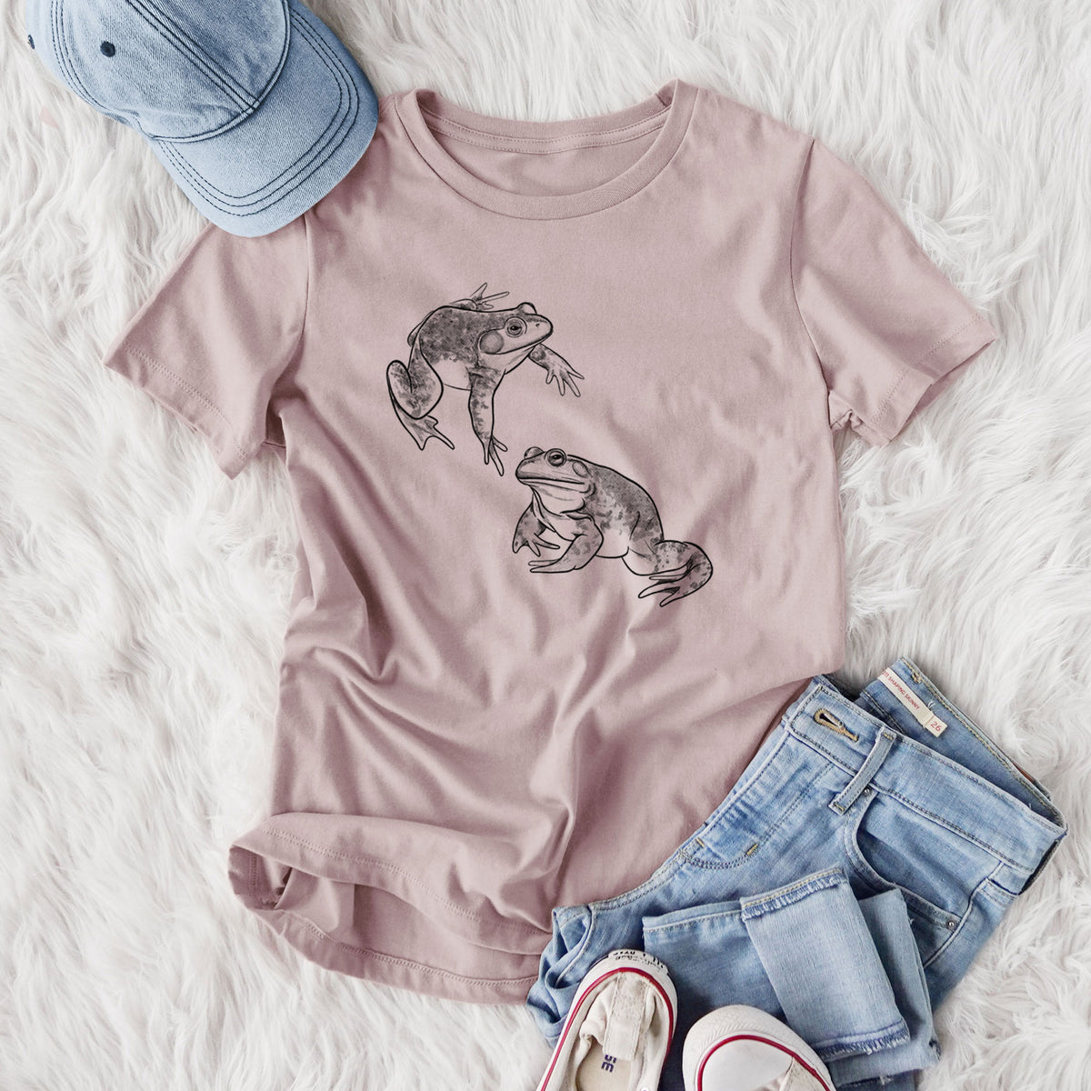 Women's relaxed fit cotton t-shirt printed with a detailed black ink illustration of two American bullfrogs, styled flat on a white faux fur rug with jeans.