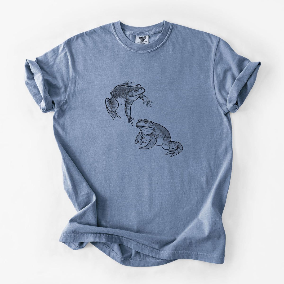 Blue jean Comfort Colors t-shirt laid flat, printed with a detailed black ink illustration of two American bullfrogs.