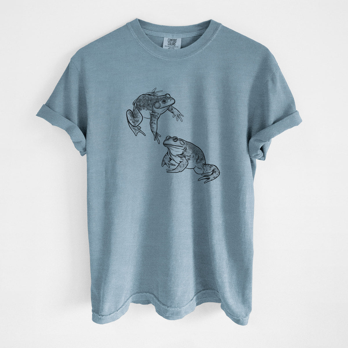 Steel blue Comfort Colors t-shirt laid flat, printed with a detailed black ink illustration of two American bullfrogs.