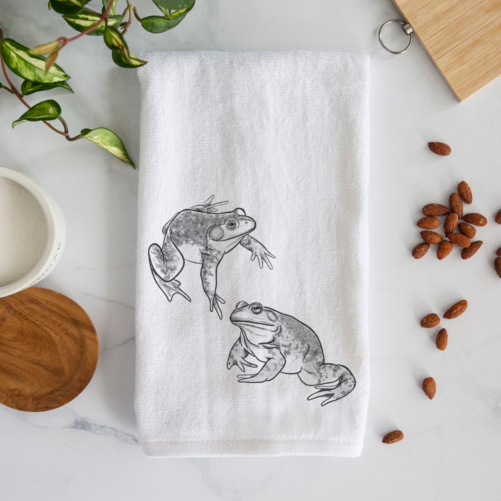 White hand towel printed with a detailed black ink illustration of two American bullfrogs.