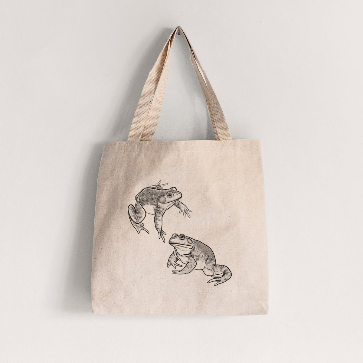 Natural canvas tote bag printed with a detailed black ink illustration of two American bullfrogs.