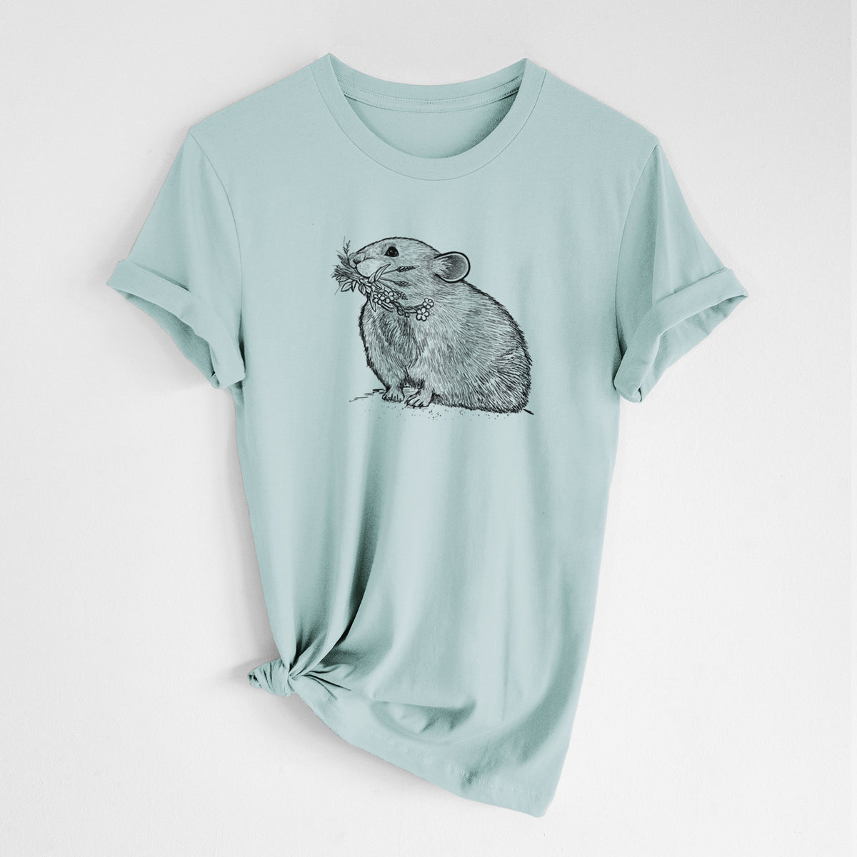 Dusty blue lightweight cotton t-shirt laid flat with the sleeves rolled, printed with a detailed black ink illustration of an American pika holding flowers and grass in its mouth.