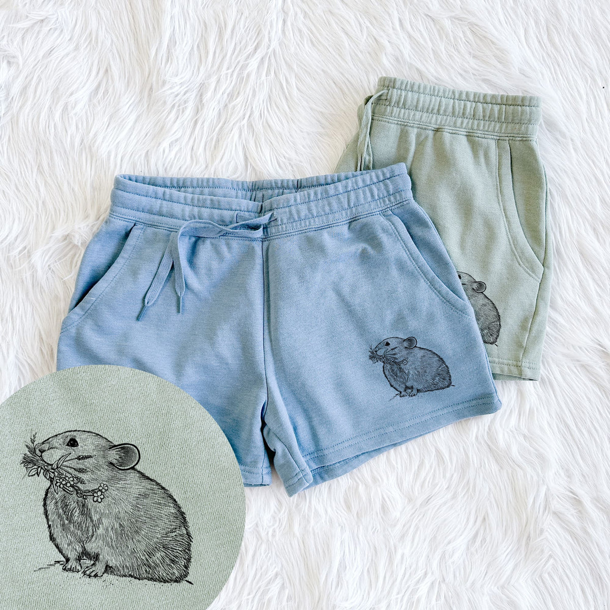 Two pairs of Cali Wave shorts in different colors printed with a detailed black ink illustration of an American pika holding flowers and grass in its mouth, with a close-up of the print.