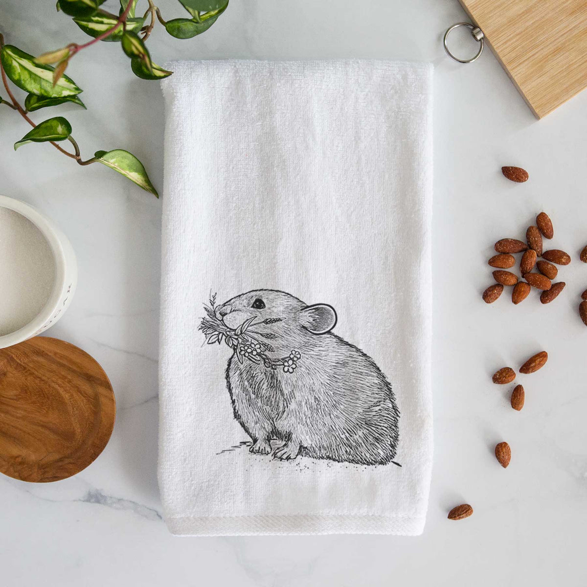 White hand towel printed with a detailed black ink illustration of an American pika holding flowers and grass in its mouth.