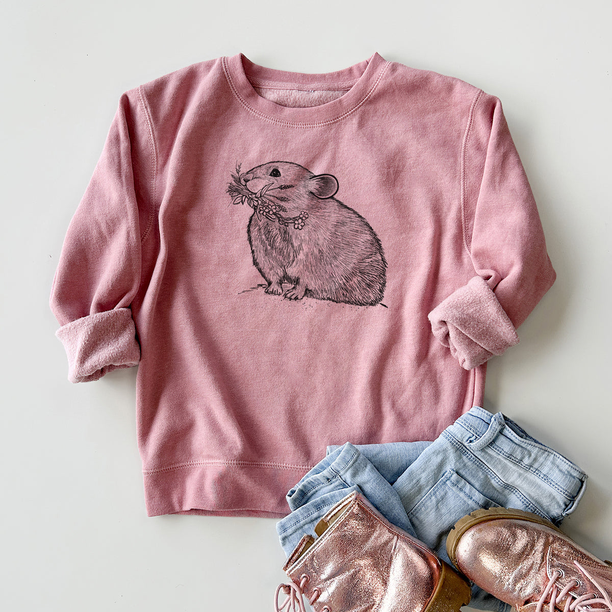 Youth crewneck sweatshirt printed with a detailed black ink illustration of an American pika holding flowers and grass in its mouth, styled flat with jeans and boots.