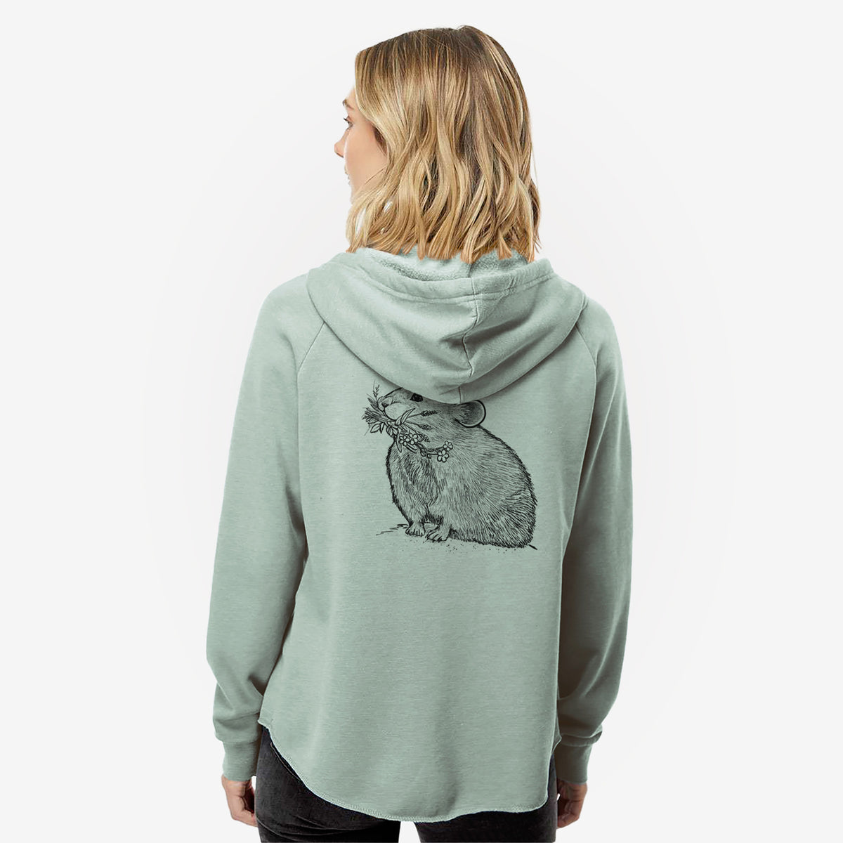 Woman wearing a sage green women's Cali Wave zip-up sweatshirt printed with a detailed black ink illustration of an American pika holding flowers and grass in its mouth, seen from behind.