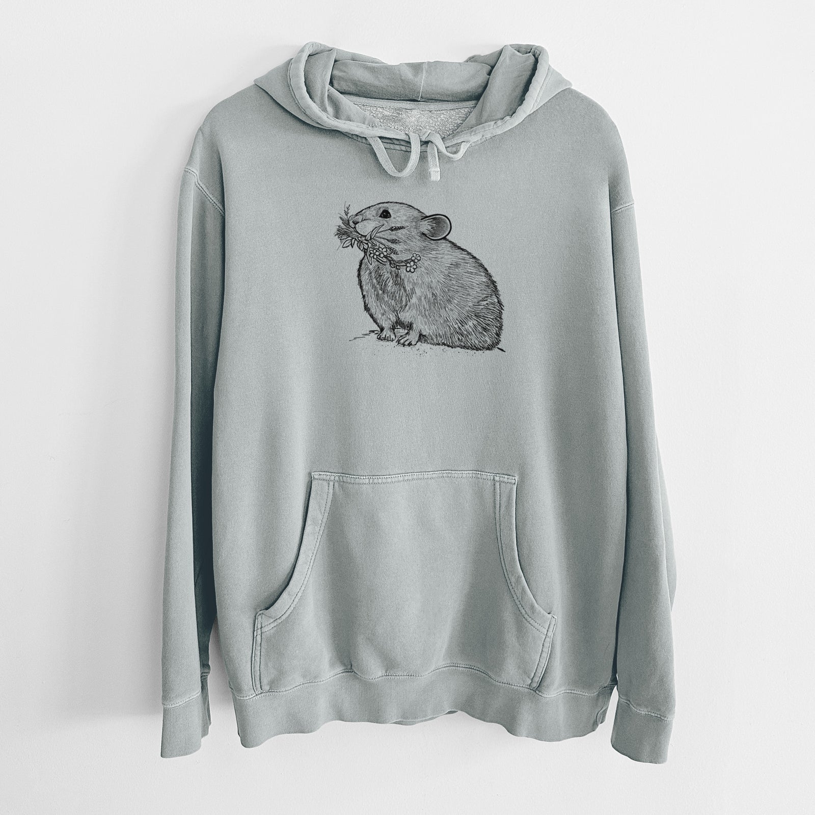 Sage green pigment dyed hoodie laid flat, printed with a detailed black ink illustration of an American pika holding flowers and grass in its mouth.