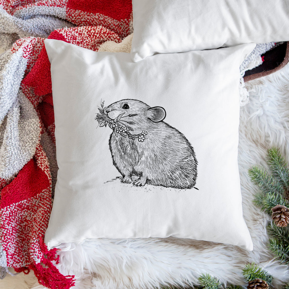 White pillow cover printed with a detailed black ink illustration of an American pika holding flowers and grass in its mouth, on a woven chair.
