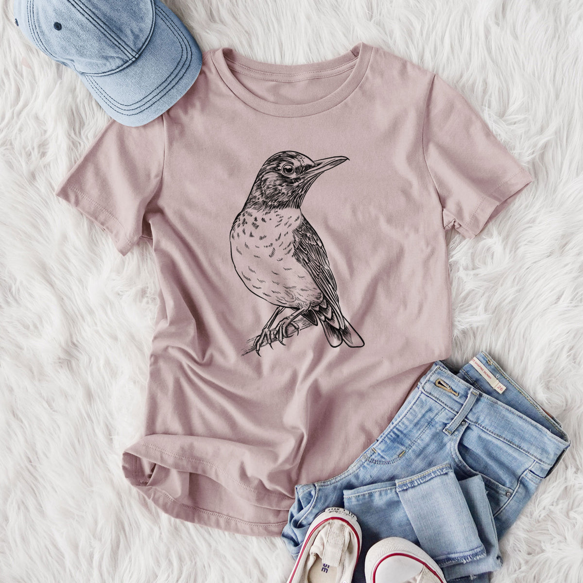 Women's relaxed fit cotton t-shirt printed with a detailed black ink sketch of an American robin perched on a branch, styled flat on a white faux fur rug with jeans.