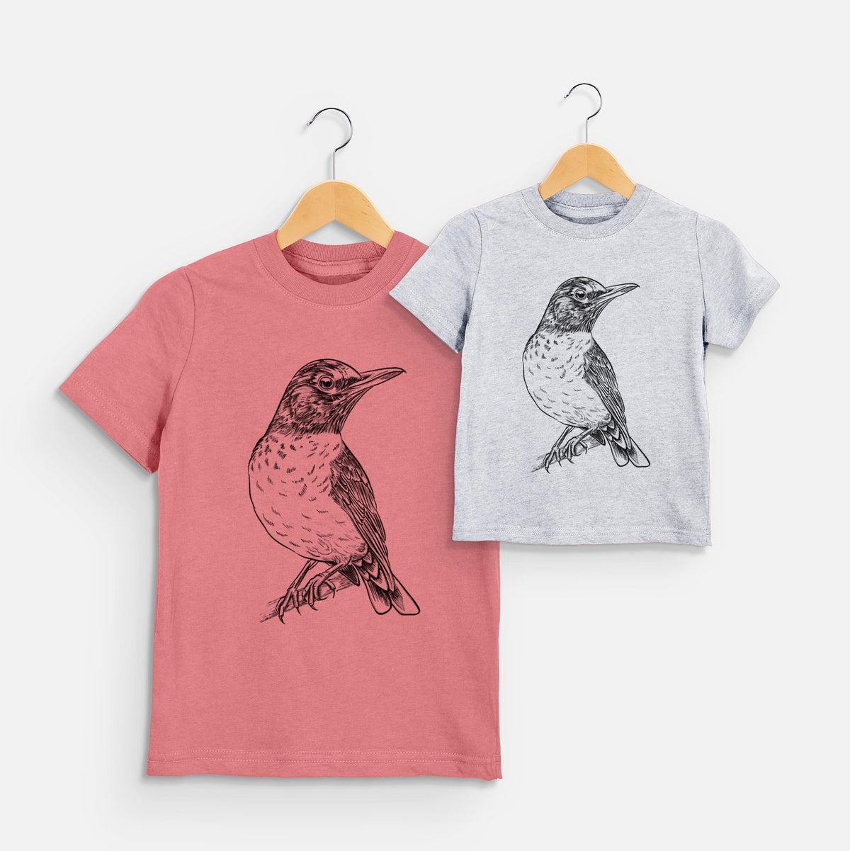 Two youth t-shirts in different colors on hangers, printed with a detailed black ink sketch of an American robin perched on a branch.