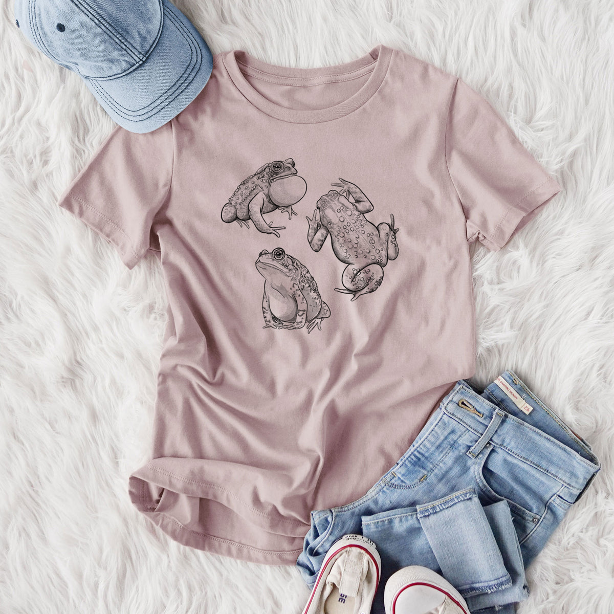 Women's relaxed fit cotton t-shirt printed with a black ink illustration of three American toads, styled flat on a white faux fur rug with jeans.