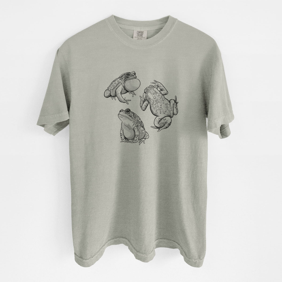 Sandstone beige Comfort Colors t-shirt laid flat, printed with a black ink illustration of three American toads.