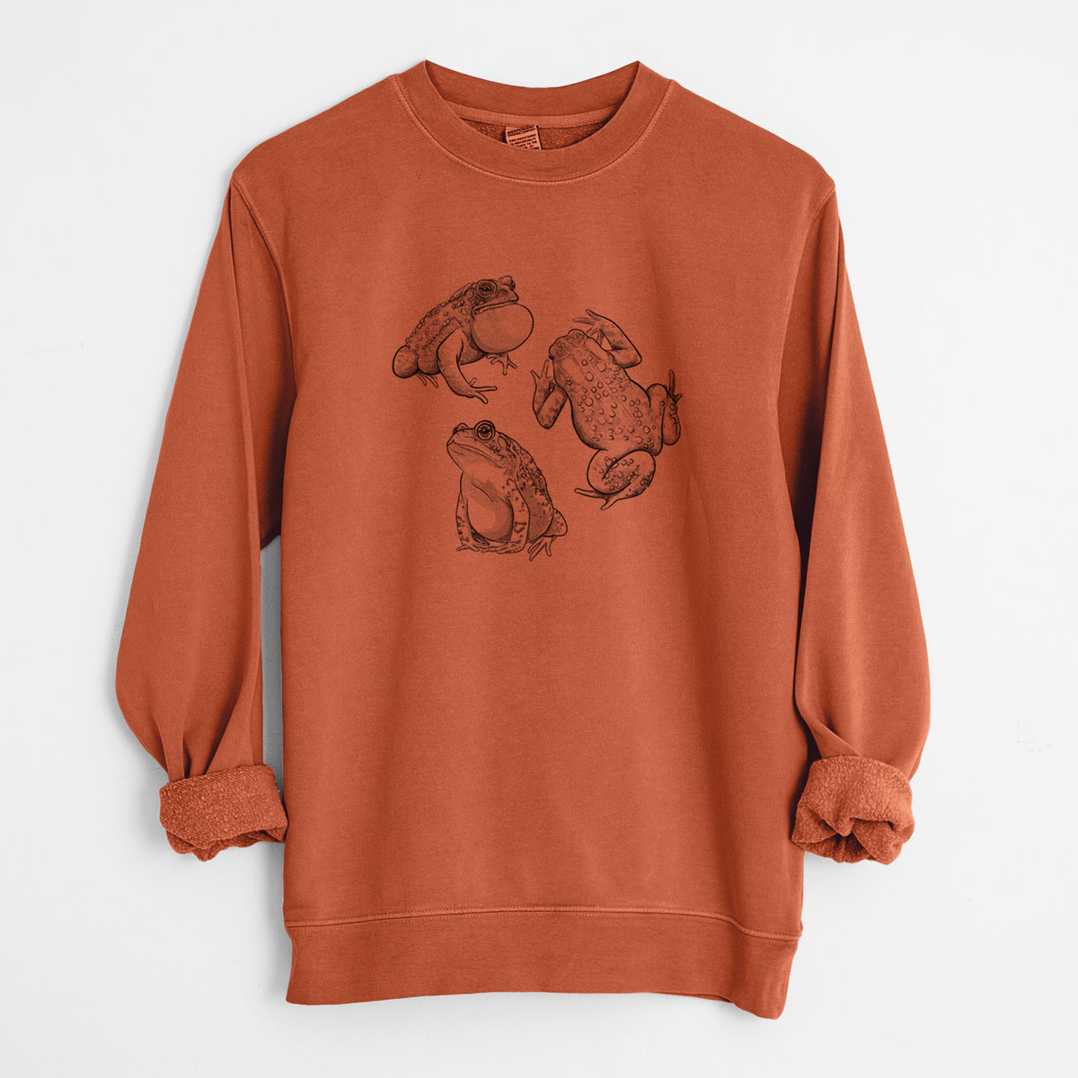 Amber orange pigment dyed crewneck sweatshirt laid flat with the sleeves rolled, printed with a black ink illustration of three American toads.
