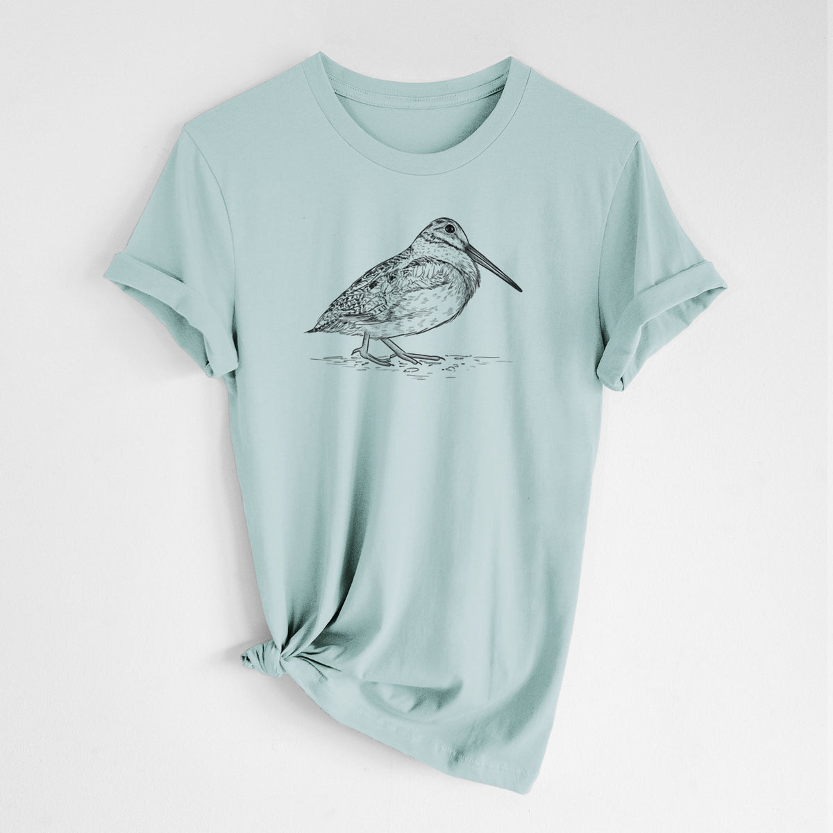 Dusty blue lightweight cotton t-shirt laid flat with the sleeves rolled, printed with a detailed black ink sketch of an American woodcock standing on the ground.