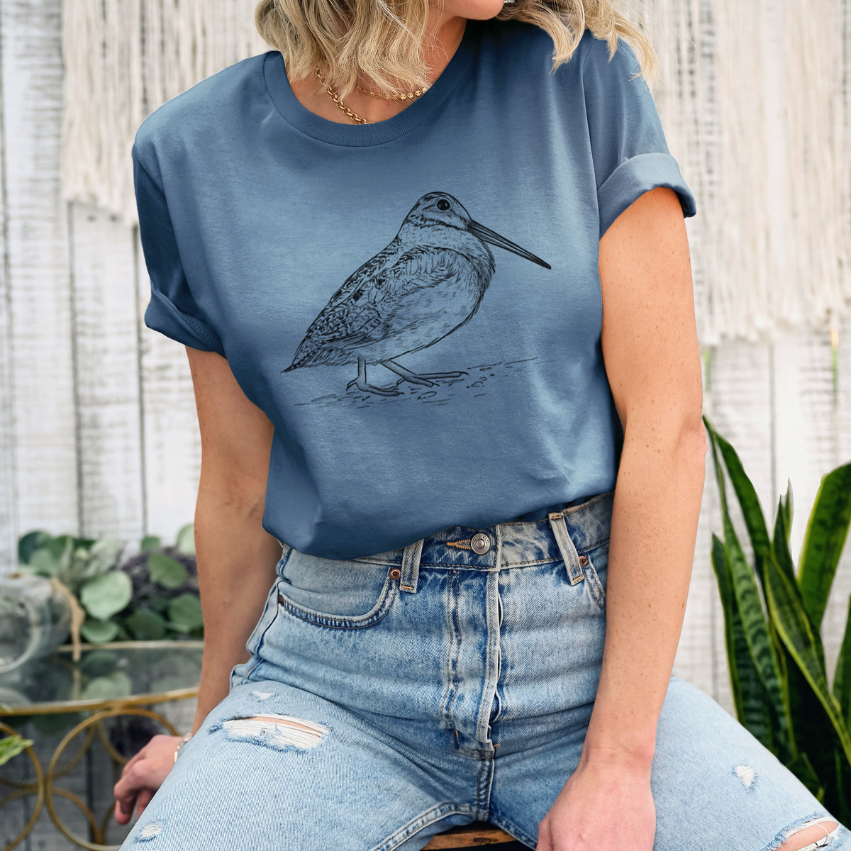 Woman wearing a steel blue lightweight cotton t-shirt printed with a detailed black ink sketch of an American woodcock standing on the ground.