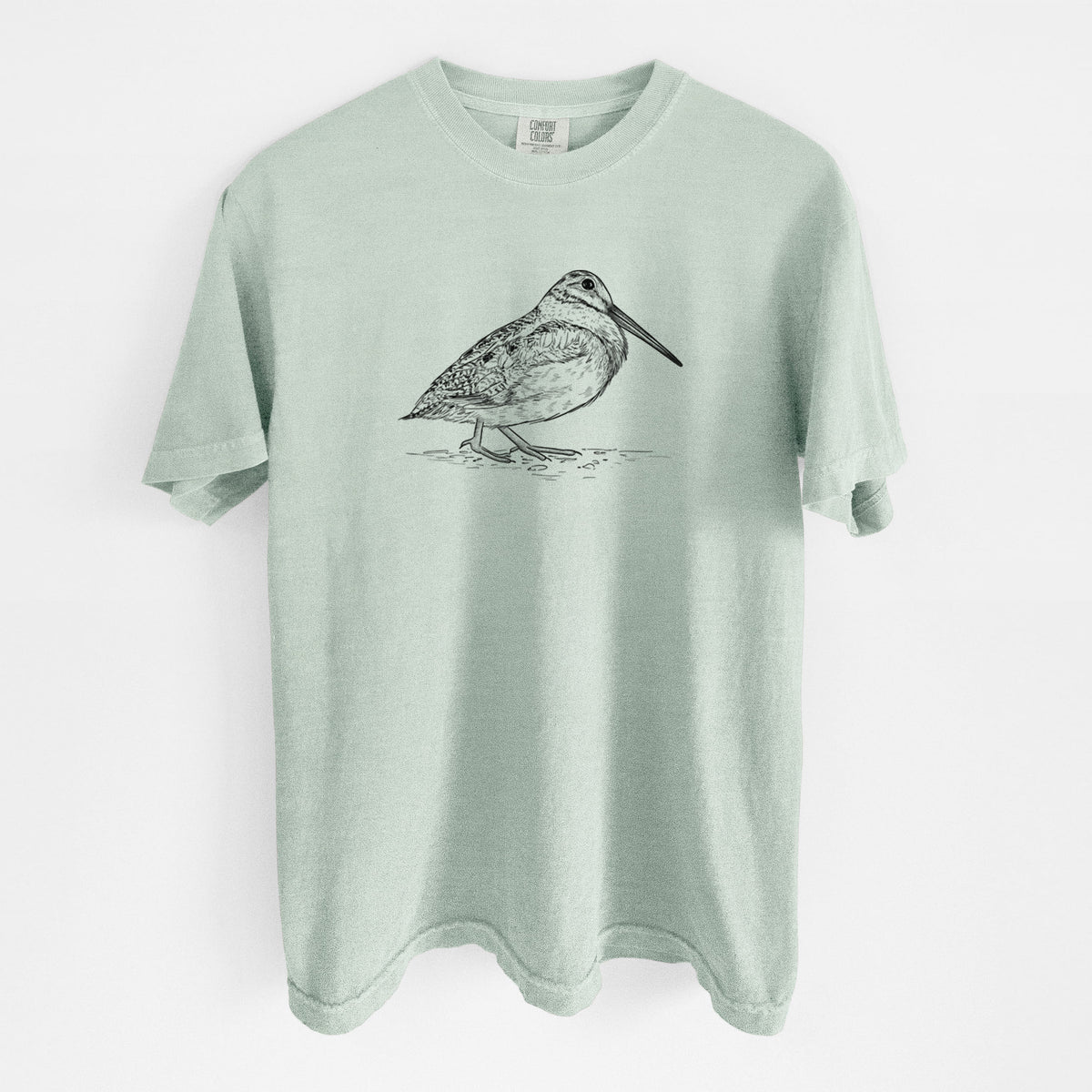 Bay green Comfort Colors t-shirt laid flat, printed with a detailed black ink sketch of an American woodcock standing on the ground.