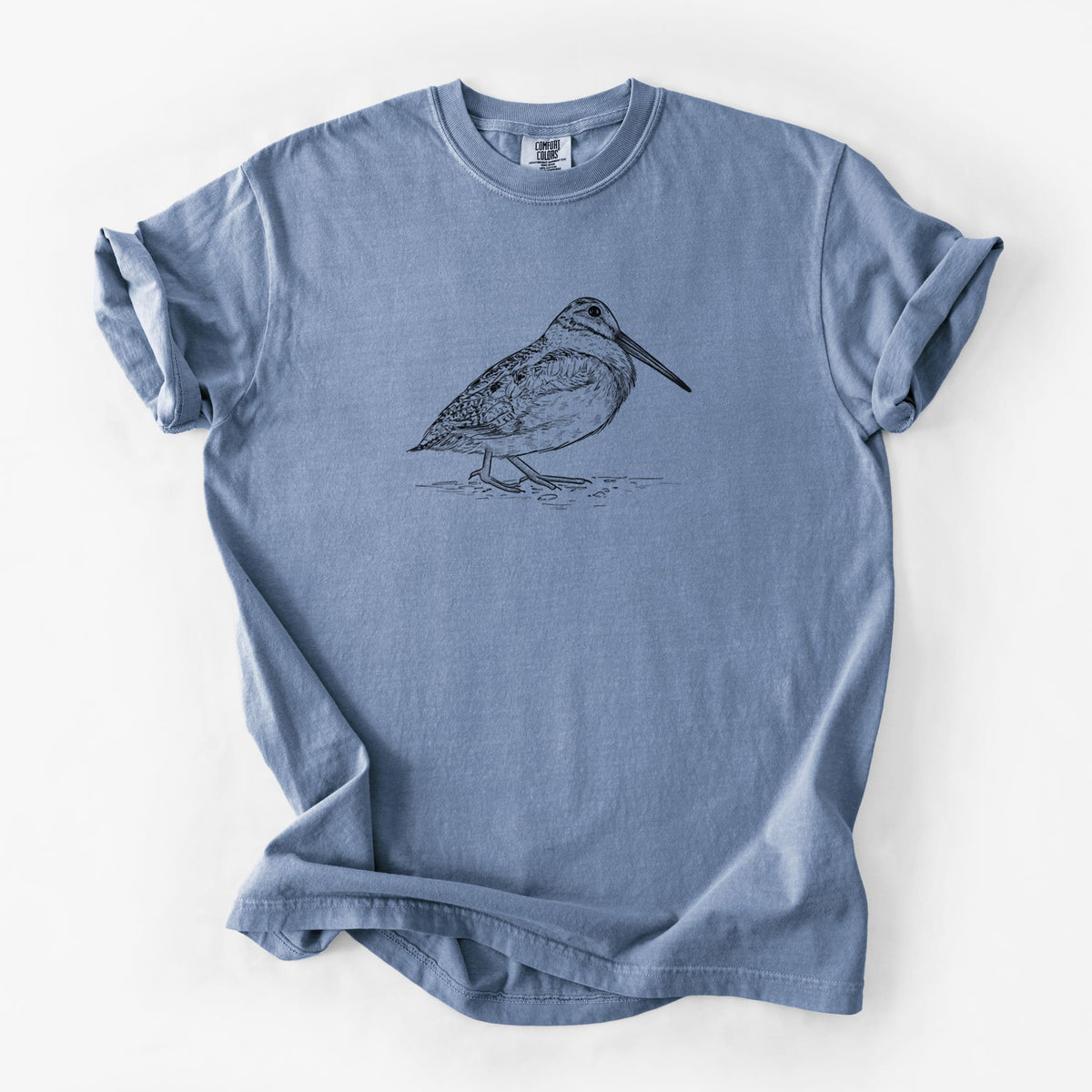 Blue jean Comfort Colors t-shirt laid flat, printed with a detailed black ink sketch of an American woodcock standing on the ground.