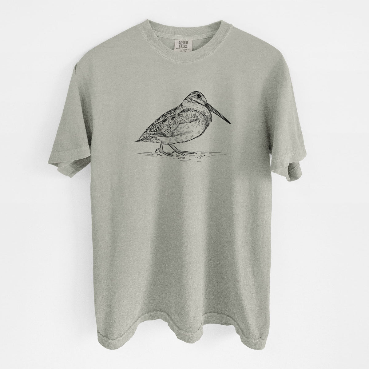 Sandstone beige Comfort Colors t-shirt laid flat, printed with a detailed black ink sketch of an American woodcock standing on the ground.