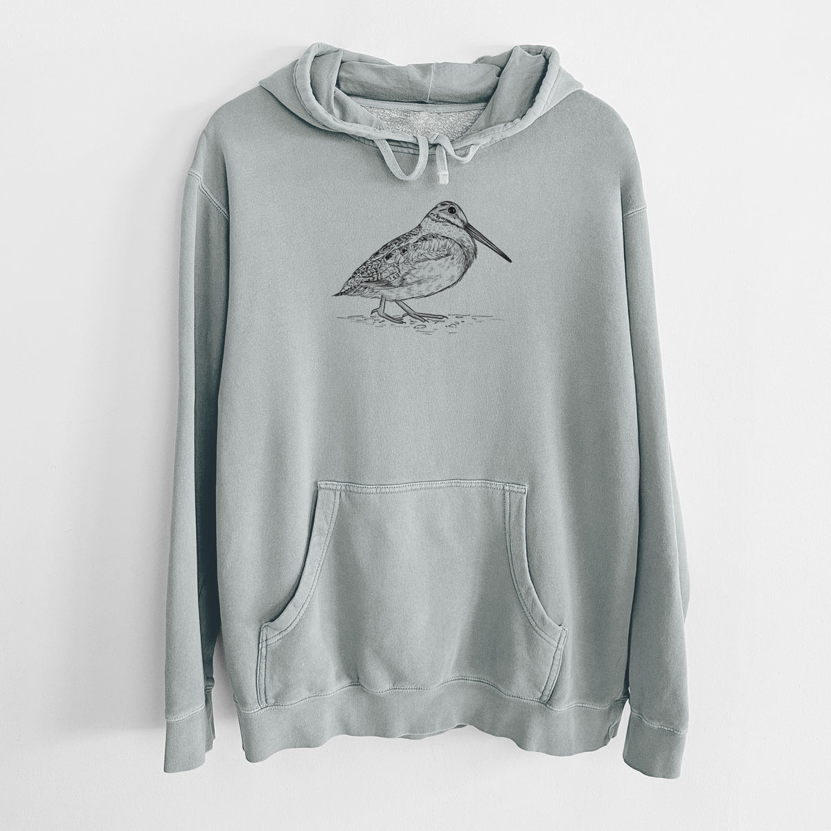 Sage green pigment dyed hoodie laid flat, printed with a detailed black ink sketch of an American woodcock standing on the ground.