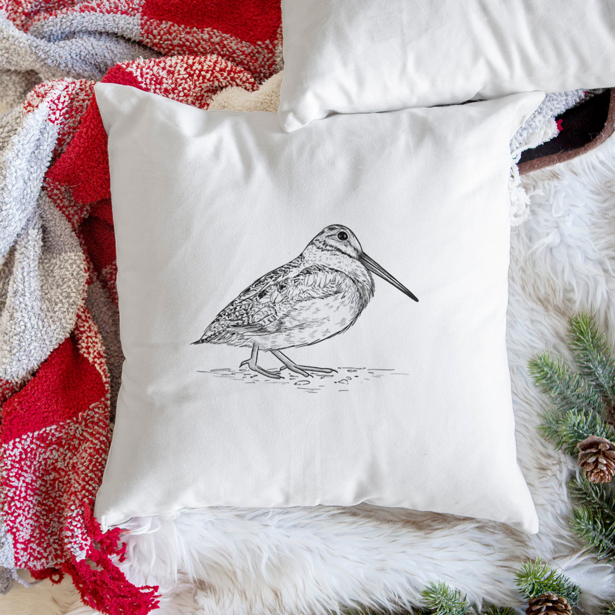 White pillow cover printed with a detailed black ink sketch of an American woodcock standing on the ground, on a woven chair.