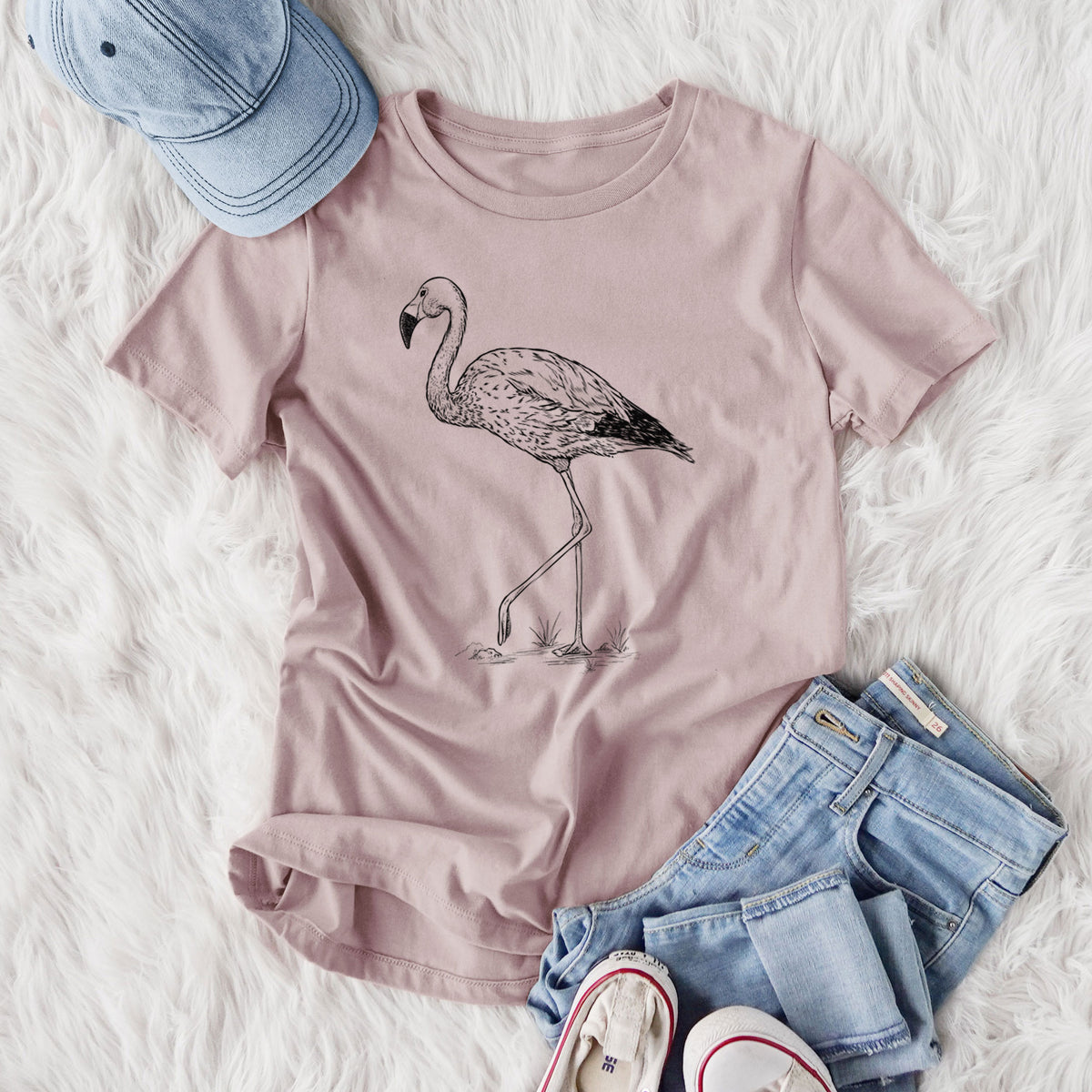 Women's relaxed fit cotton t-shirt printed with a black ink illustration of an Andean flamingo standing on one leg, styled flat on a white faux fur rug with jeans.