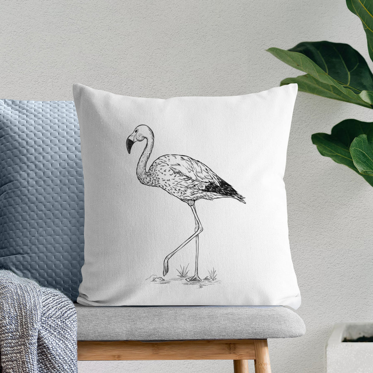 White pillow cover printed with a black ink illustration of an Andean flamingo standing on one leg, on a bench beside plants.