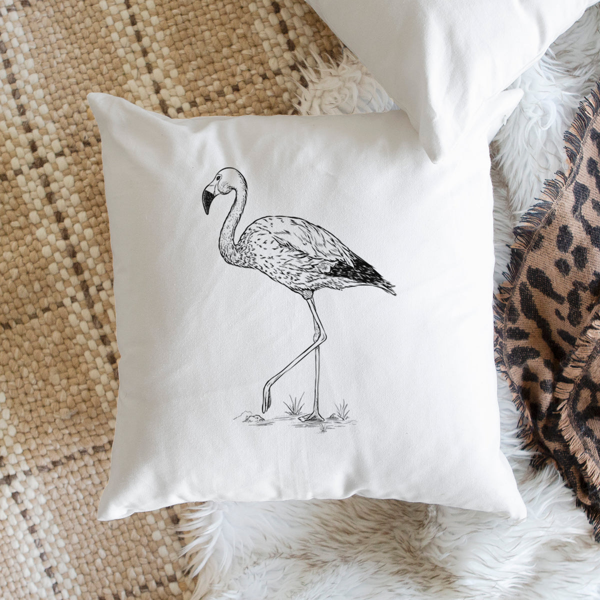 White pillow cover printed with a black ink illustration of an Andean flamingo standing on one leg, on a woven chair.
