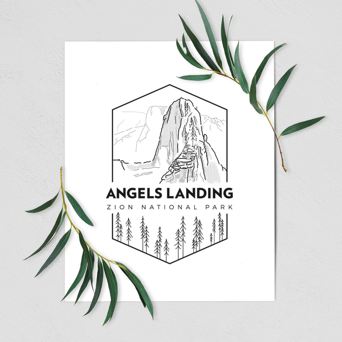 Art print of a black line art badge of Angels Landing above pine trees, with the words Angels Landing, Zion National Park, shown with eucalyptus leaves.