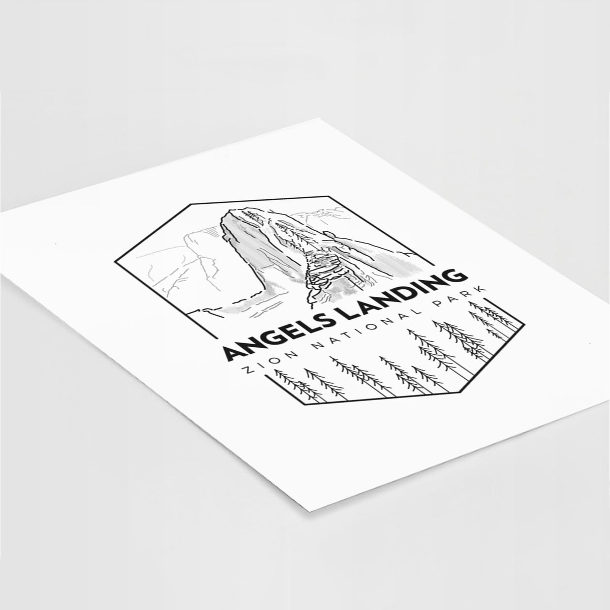Art print of a black line art badge of Angels Landing above pine trees, with the words Angels Landing, Zion National Park, lying at an angle on a white surface.