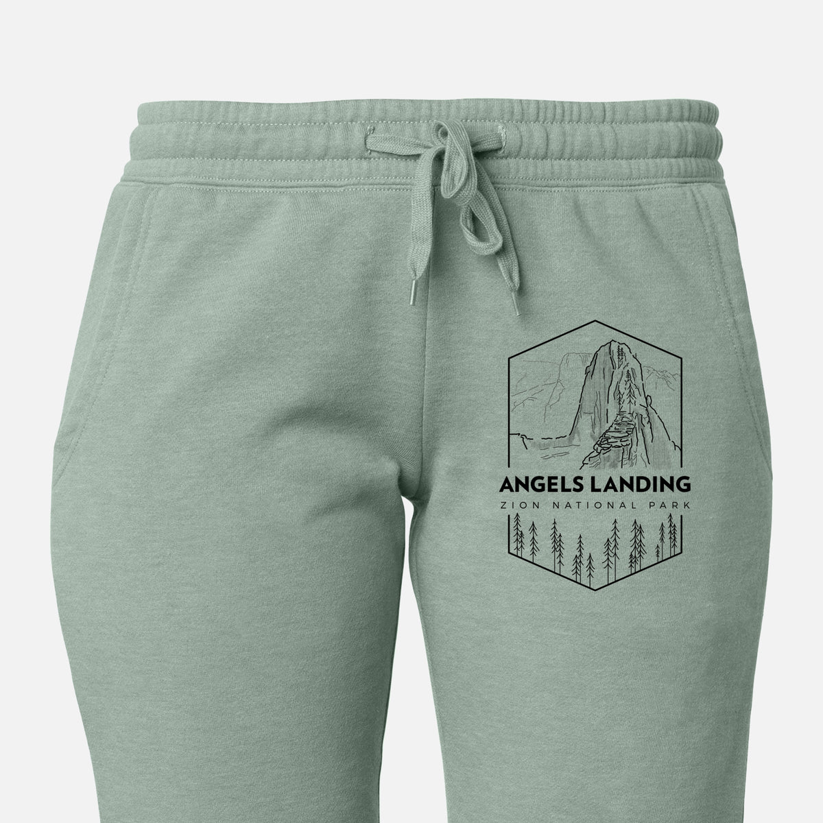 Front of sage green Cali Wave sweatpants, printed with a black line art badge of Angels Landing above pine trees, with the words Angels Landing, Zion National Park on the leg.