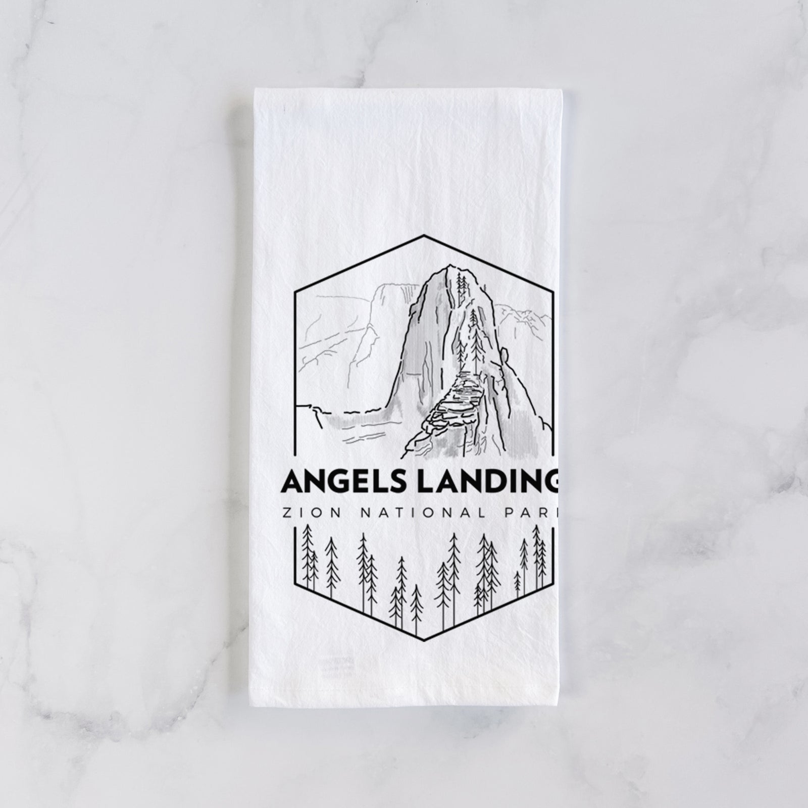 White cotton tea towel printed with a black line art badge of Angels Landing above pine trees, with the words Angels Landing, Zion National Park, on a marble counter beside a round wooden cutting board and greenery.