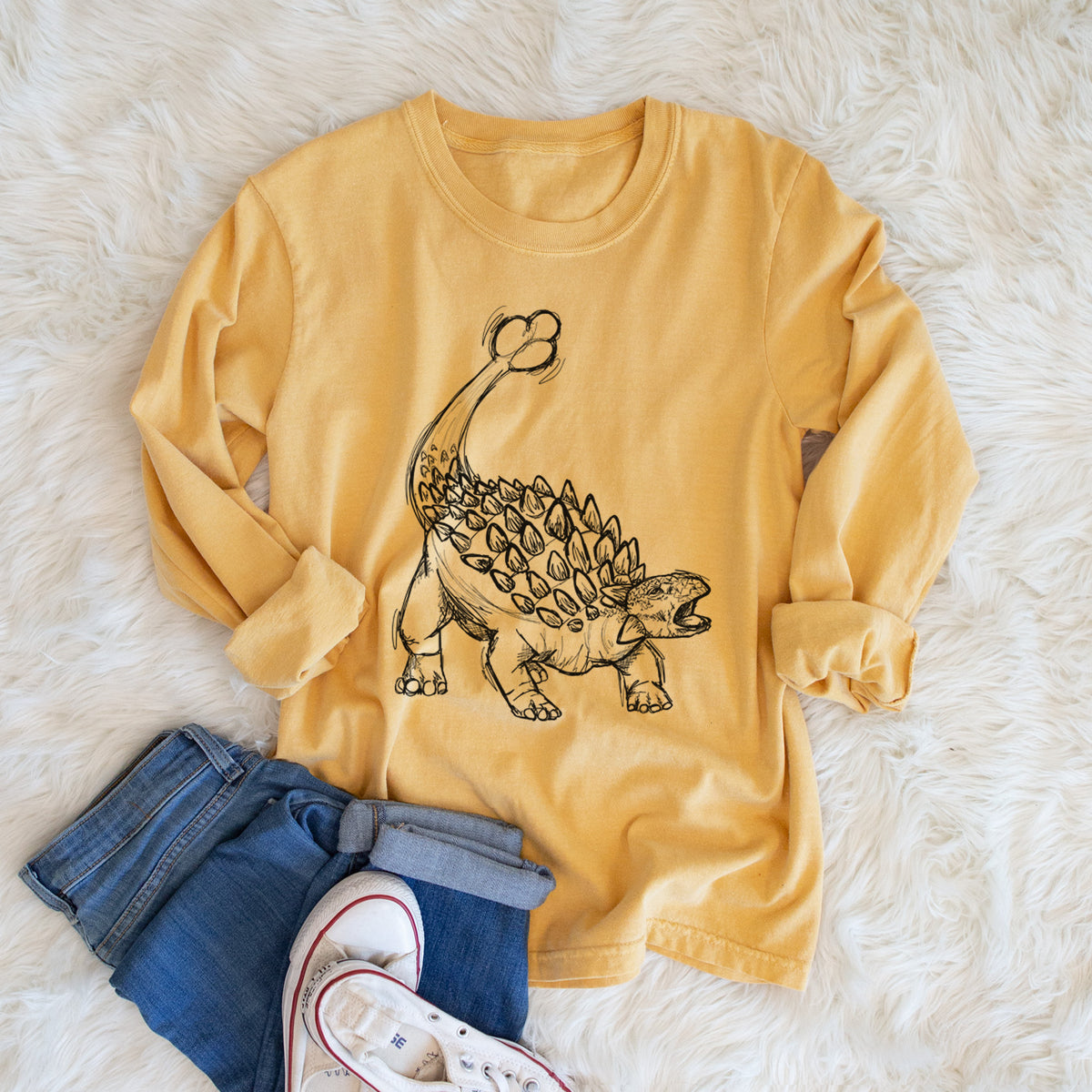 Golden wheat yellow Comfort Colors long sleeve shirt printed with a black ink illustration of an Ankylosaurus with its club tail raised, shown in a lifestyle photo.