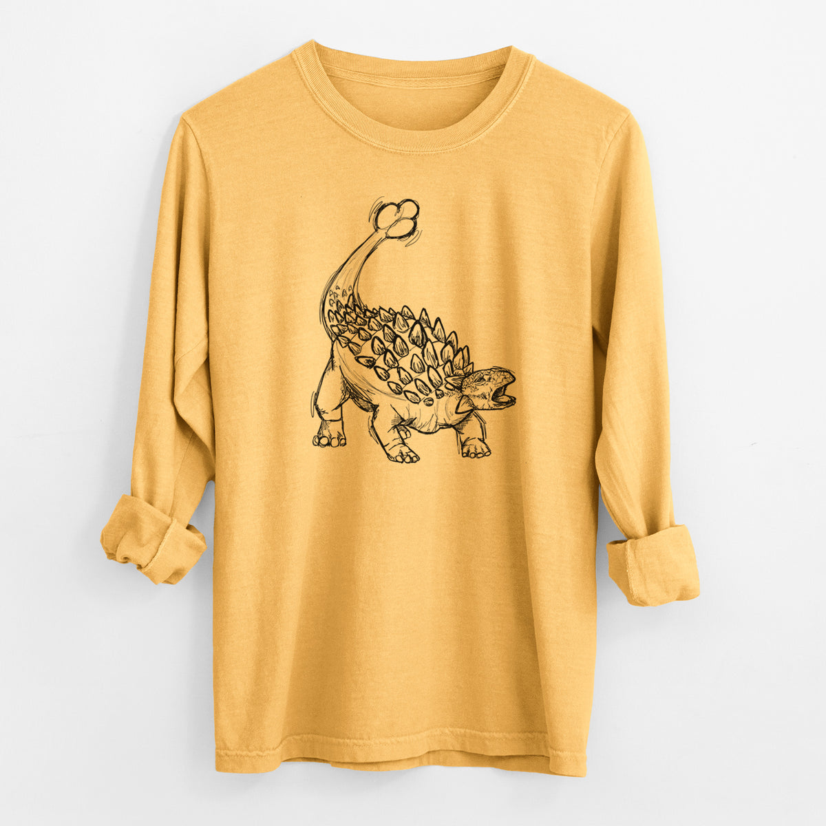 Golden wheat yellow Comfort Colors long sleeve shirt laid flat with the cuffs rolled, printed with a black ink illustration of an Ankylosaurus with its club tail raised.