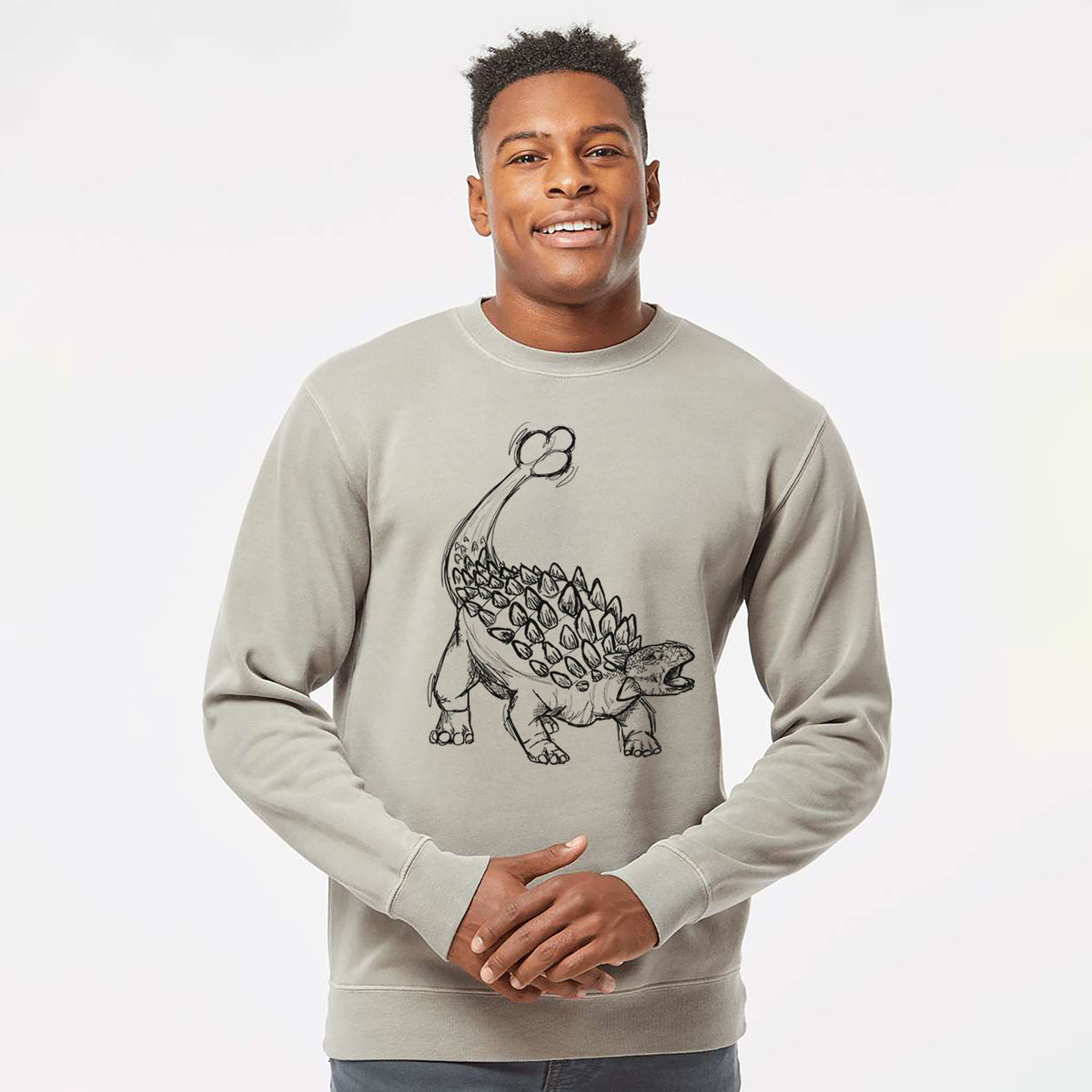 Model wearing a cement grey pigment dyed crewneck sweatshirt printed with a black ink illustration of an Ankylosaurus with its club tail raised.
