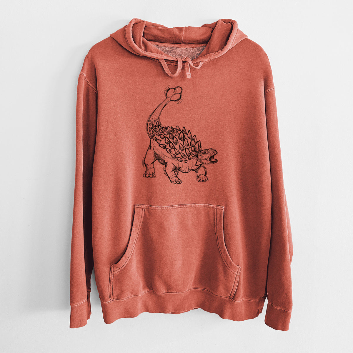 Amber orange pigment dyed hoodie laid flat, printed with a black ink illustration of an Ankylosaurus with its club tail raised.