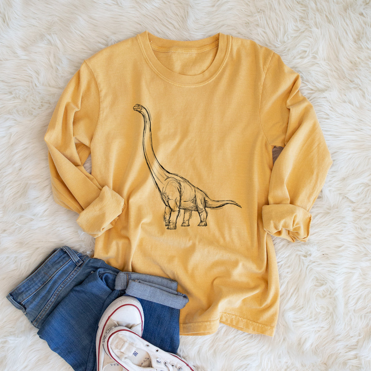 Golden wheat yellow Comfort Colors long sleeve shirt printed with a black ink illustration of a long-necked Apatosaurus walking, shown in a lifestyle photo.
