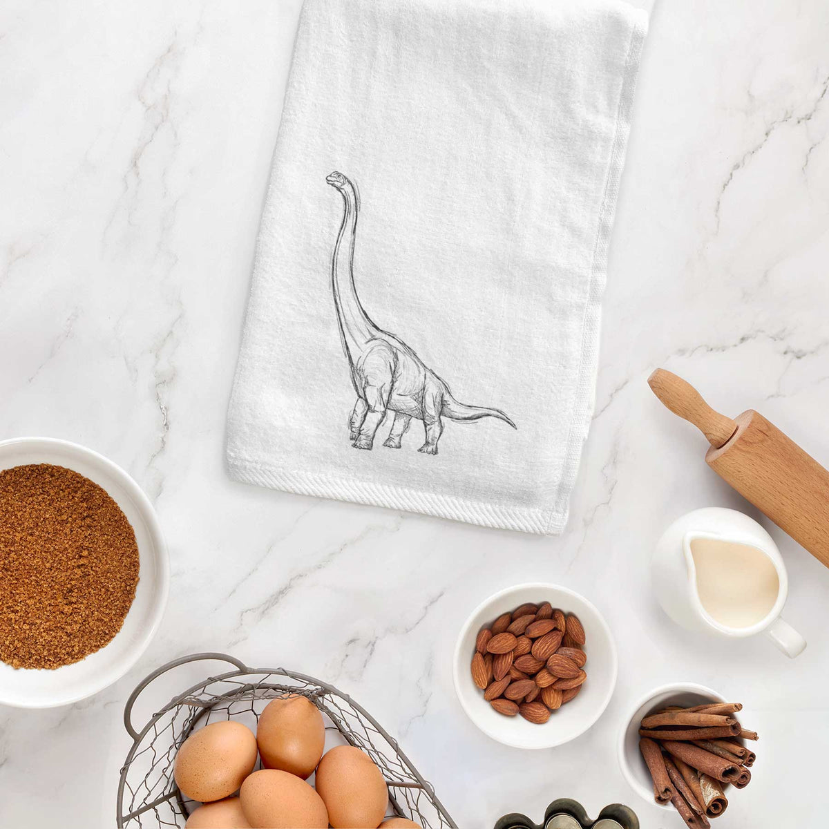 White hand towel printed with a black ink illustration of a long-necked Apatosaurus walking, hanging on a cabinet door.