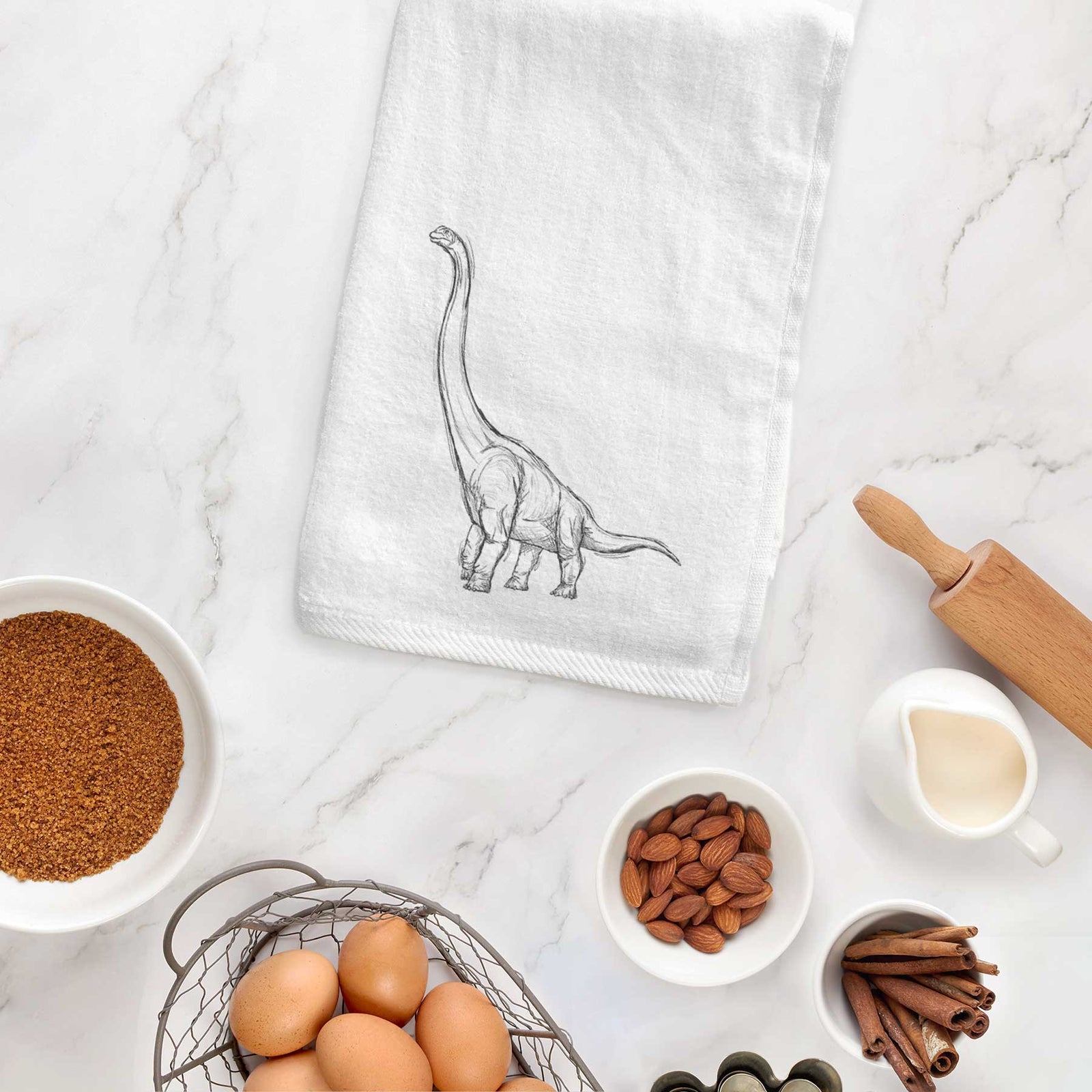 White hand towel printed with a black ink illustration of a long-necked Apatosaurus walking.
