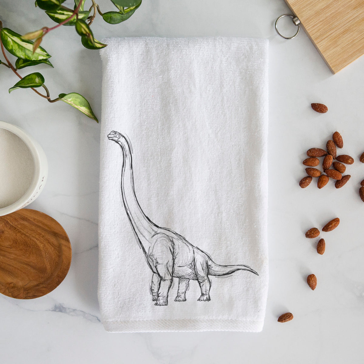 White hand towel printed with a black ink illustration of a long-necked Apatosaurus walking.