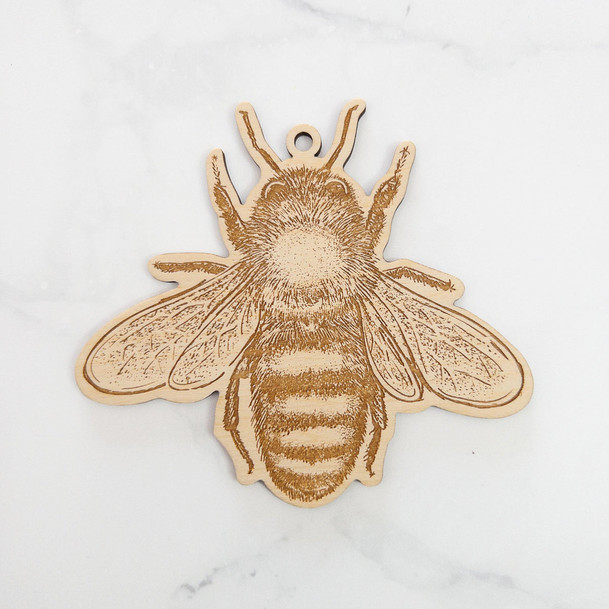 Wooden ornament featuring a detailed engraving of a honey bee, seen from above, on a marble surface.