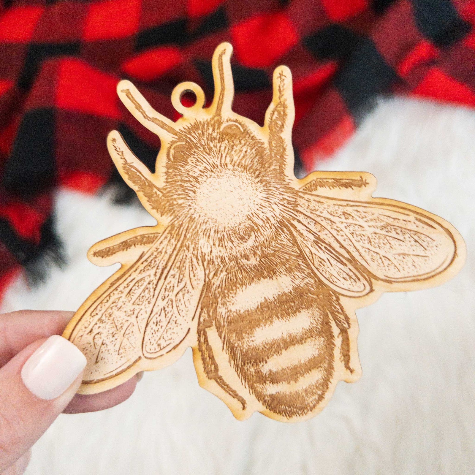 Wooden ornament featuring a detailed engraving of a honey bee, seen from above, on a knit blanket with pine cones.
