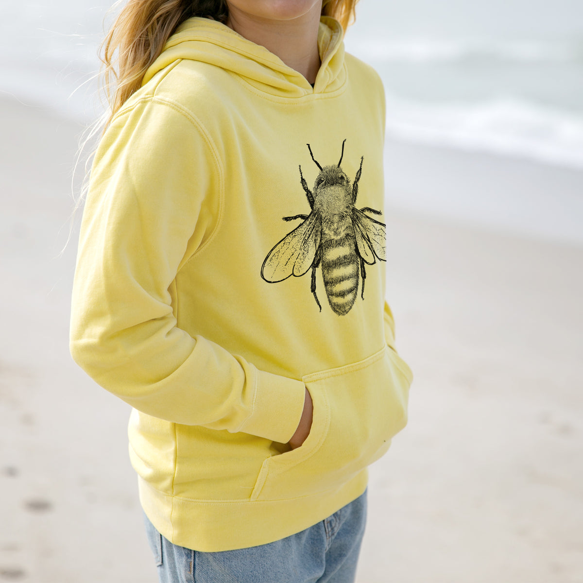 Girl wearing a youth pigment dyed hoodie printed with a detailed black ink illustration of a honey bee with its wings spread, seen from above.