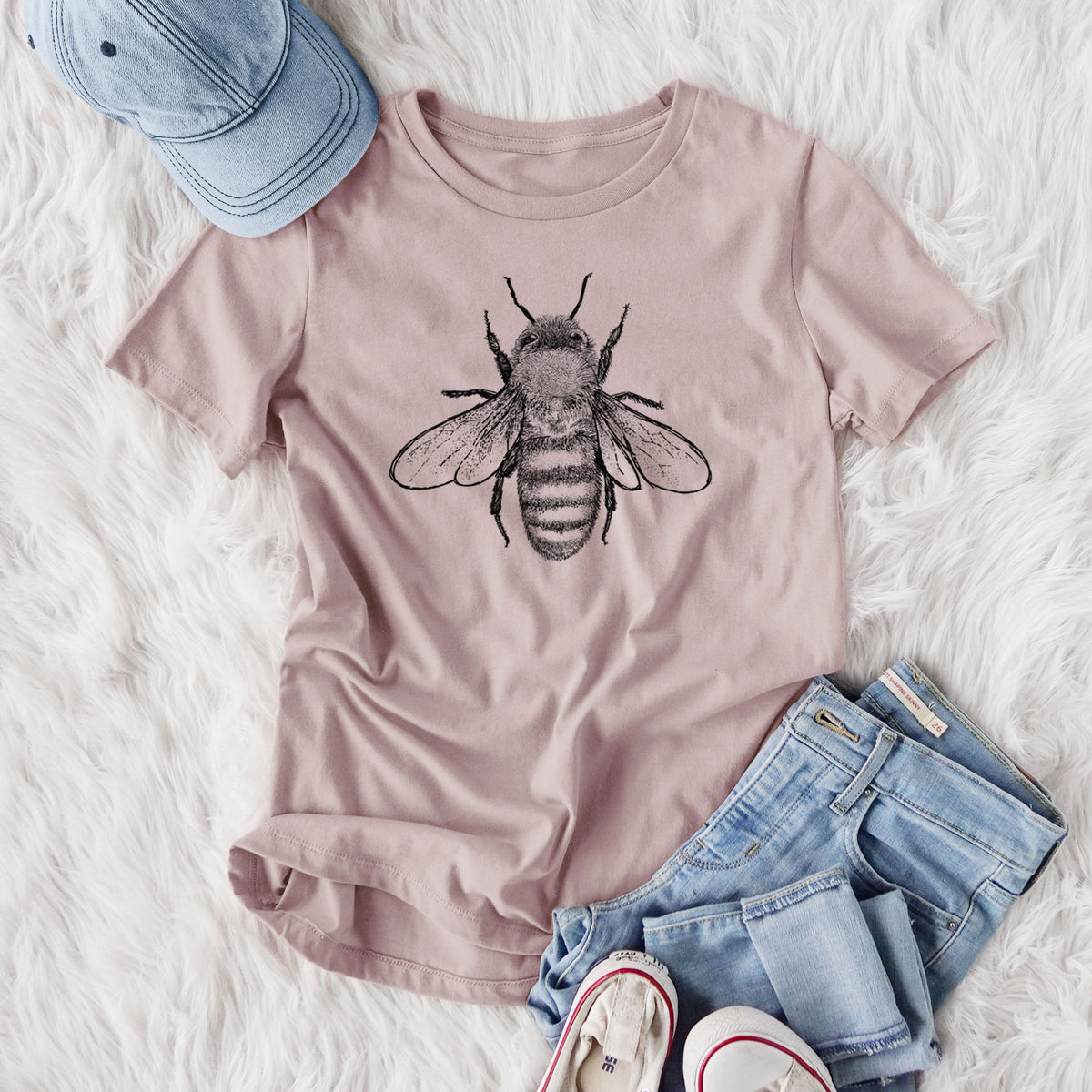 Women's relaxed fit cotton t-shirt printed with a detailed black ink illustration of a honey bee with its wings spread, seen from above, styled flat on a white faux fur rug with jeans.