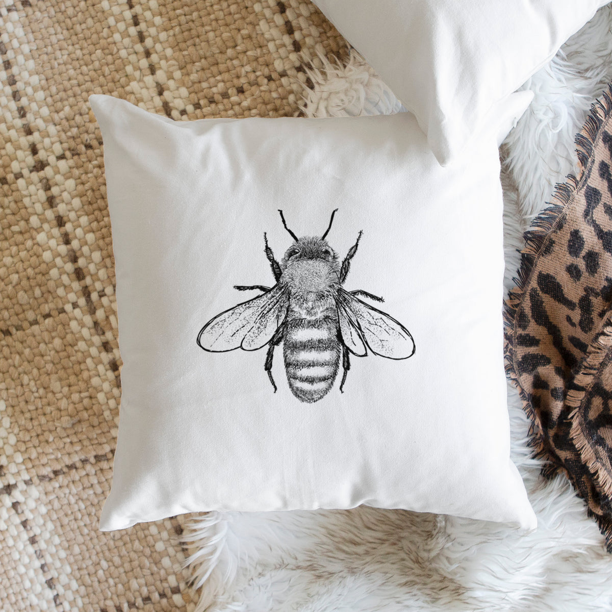 White pillow cover printed with a detailed black ink illustration of a honey bee with its wings spread, seen from above, on a woven chair.